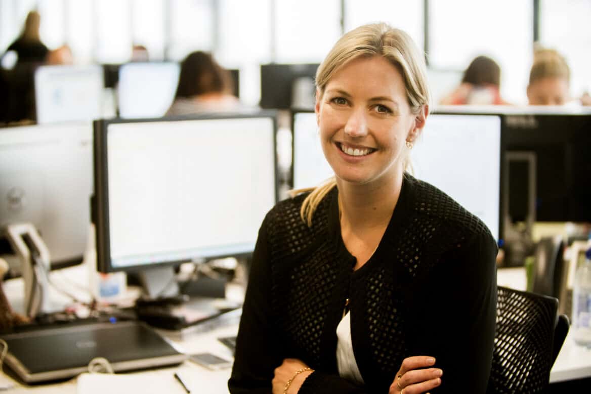 Woman sitting at computer workstation, smiling, arms crossed